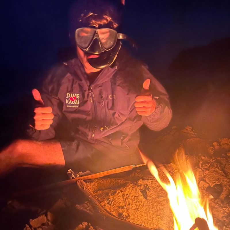 a man giving a thumbs up next to a small bonfire on the beach